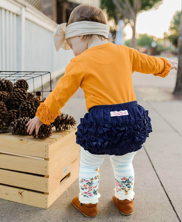 Baby girl wearing dark wash woven RuffleButt Bloomer with ruffle details, designed for kids and baby girls by RuffleButts + RuggedButts