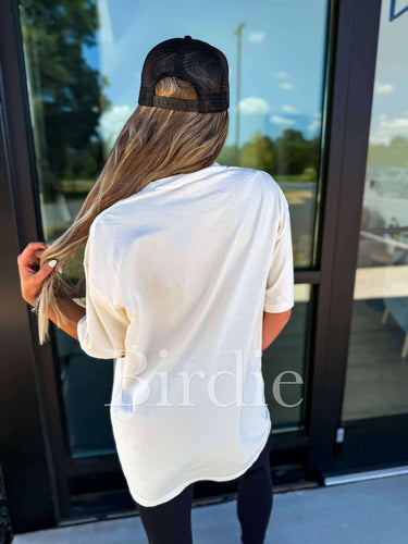 Birdie Shoulda Been A Cowghoul ivory graphic T-shirt with spooky cow skull illustration on soft cotton fabric.