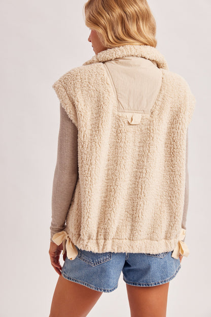 Women’s Sherpa button-down vest by blueivy, displayed on a hanger, featuring a cozy cream-colored sherpa fabric and button closure.