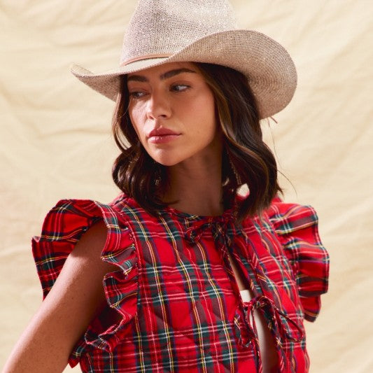 Woman wearing a red plaid top and cowboy hat against a beige background