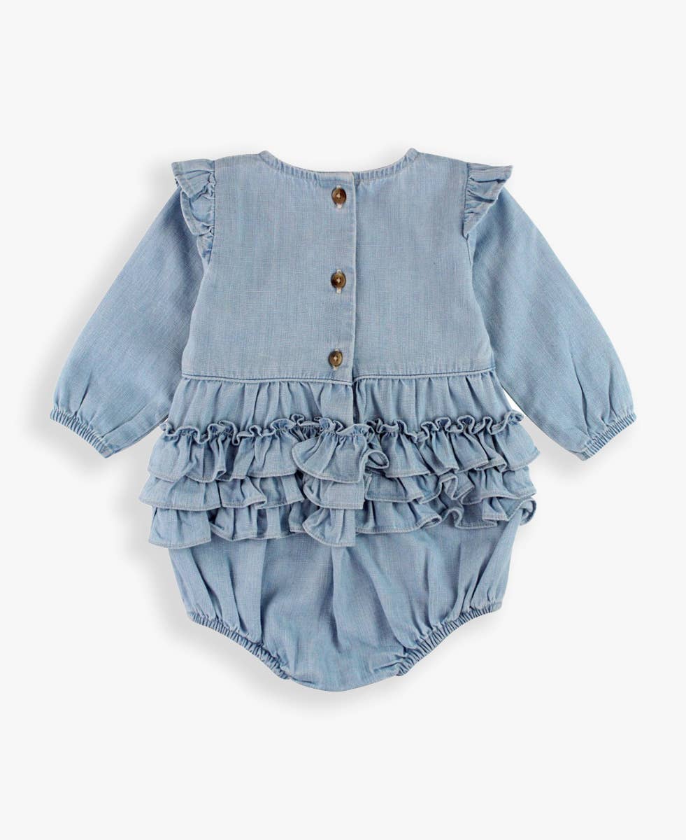 Baby girl wearing a light wash long sleeve flutter bubble romper by RuffleButts + RuggedButts, showcasing soft fabric and flutter sleeve details.