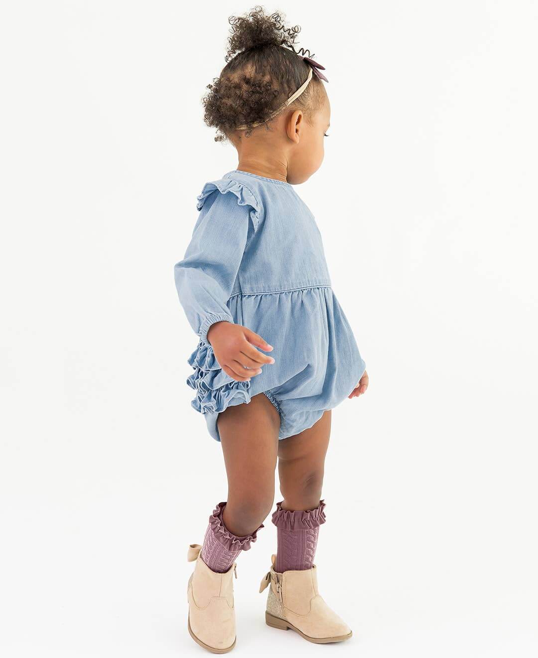 Baby girl in light wash long sleeve flutter bubble romper by RuffleButts + RuggedButts, showing adorable baby clothing for kids and babies.