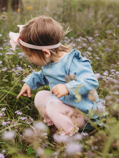 Baby girl wearing a light wash long sleeve flutter bubble romper by RuffleButts + RuggedButts, showing the cute, soft fabric and flutter sleeves.