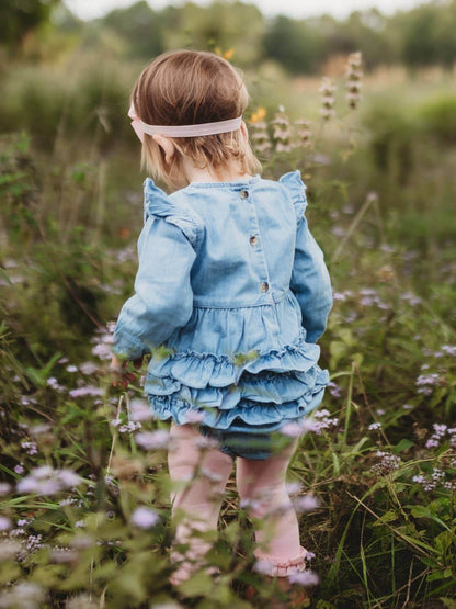 Baby girl in light wash long sleeve flutter bubble romper by RuffleButts + RuggedButts, showing the adorable design and soft fabric.