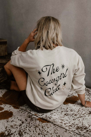 Cream-colored crewneck sweatshirt featuring "The Cowgirl Club" text in bold, casual style, from Summer Tees.